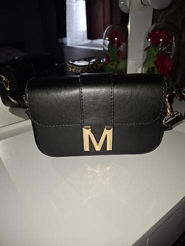 Crna ženska crossbody torbica sa preklopom i metalnim „M” logom u