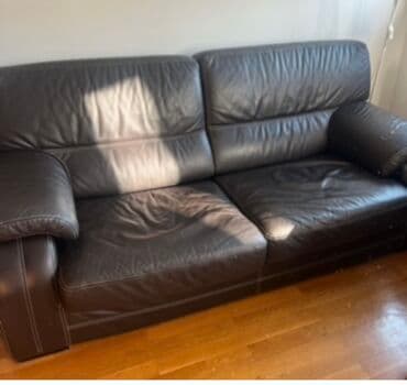 polovne garniture za dnevnu sobu: Ova udobna sofa presvučena kožom u tamnoj boji, verovatno braon ili — 1